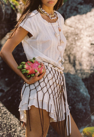 A woman sits on a sandy beach wearing a white short-sleeve top