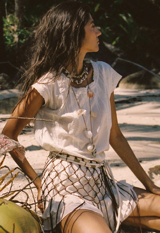  holding a pink dragon fruit. She is wearing layered gold necklaces.