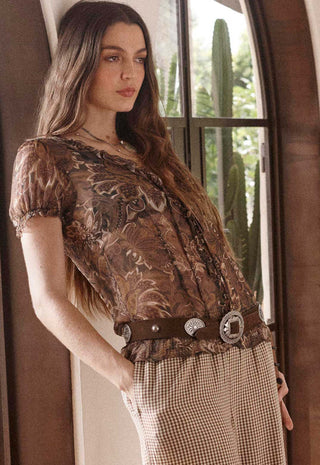 A woman wearing a brown floral lace top and a brown patterned skirt