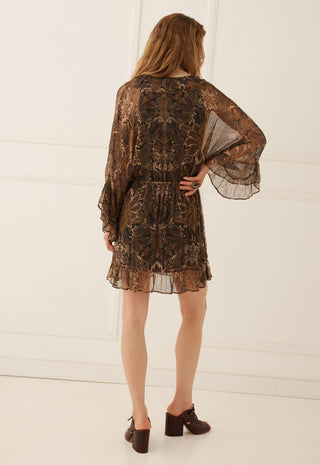 a-woman-viewed-from-behind-wearing-a-brown-sheer-lace-mini-dress-with-a-floral-pattern-and-flared-bell-sleeves-paired-with-dark-brown-block-heel-mules-set-against-a-white-paneled-wall