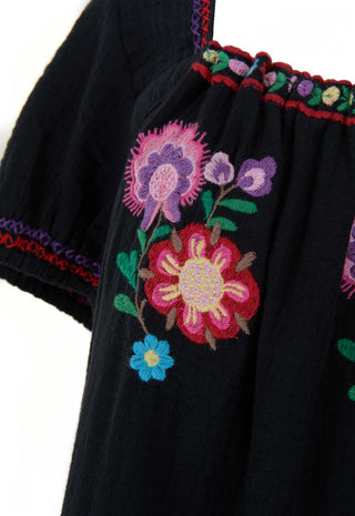 Close-up of a black embroidered blouse featuring vibrant floral patterns in pink, purple, blue, and green, with red and purple trim along the neckline.