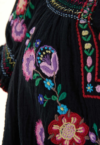Close-up of a black embroidered textile with colorful floral motifs in pink, purple, blue, green, red, and yellow, plus decorative border stitching.