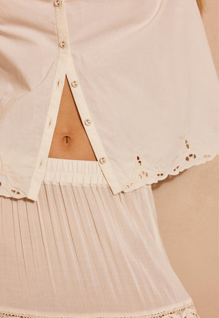 A close up of a woman modeling a cream-colored short-sleeve bohemian-style blouse and matching skirt, against a warm beige background.