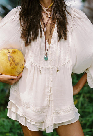  with layered necklaces and a tropical ocean background.
