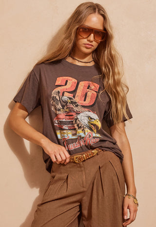 A woman wearing a brown graphic t-shirt with a racing number 26 design