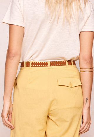 a-person-shown-from-the-back-wearing-a-cream-short-sleeve-t-shirt-a-brown-studded-belt-and-mustard-yellow-trousers-with-a-flap-pocket