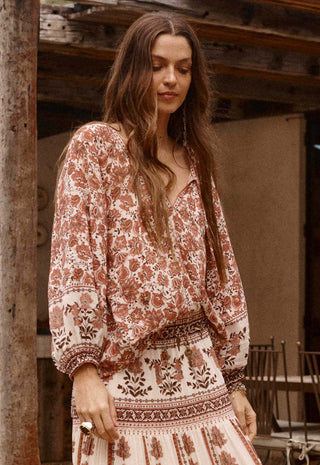 A woman wearing a bohemian-style long-sleeve maxi dress with a rust-brown and cream floral pattern