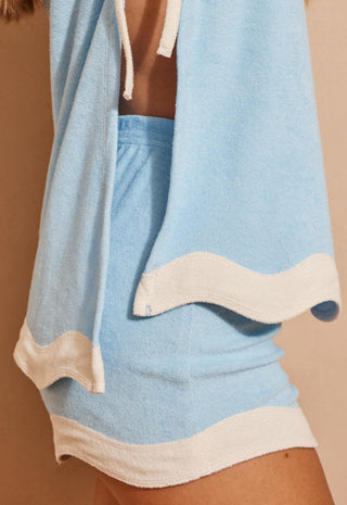 A close-up of a light blue and cream two-piece lounge set worn by a model, featuring a matching top and shorts with wavy cream trim.