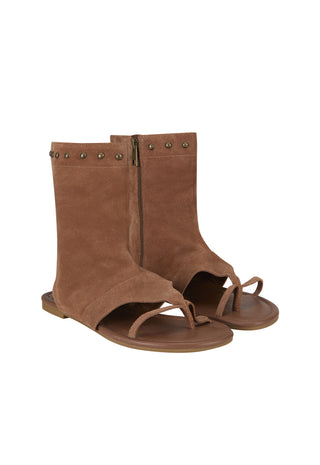 A pair of brown suede thong sandals with a mid-calf bootie upper, featuring brass-tone metal studs along the top edge and a side zipper.